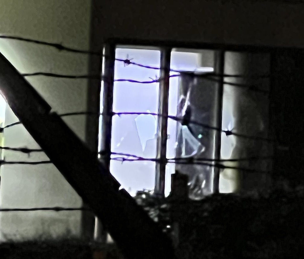 nighttime photo of a broken window seen through barbed wire